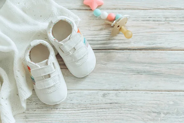 Beyaz bebek ayakkabıları ve ahşap arka planda sıcak battaniye.. — Stok fotoğraf