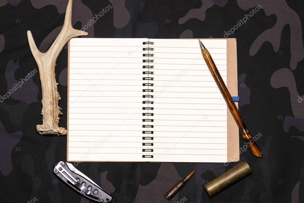 Hunting background. Blank notepad on a military camouflage background. Place for text. Flatly, top view.