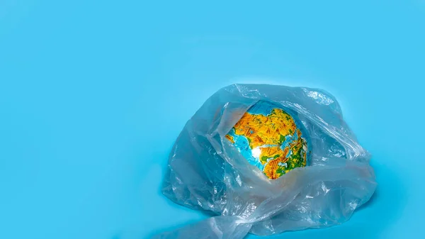 The concept of ecology. Globe in plastic wrap on a blue background. plastic waste environmental pollution concept. Place for text.