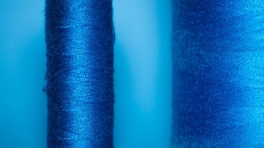 Background with a large and small blue spool of thread. They lie next to each other on a blue background.