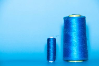 Background with a large and small blue spool of thread. They lie next to each other on a blue background.