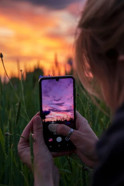 Kız cep telefonu kullanarak gün batımının fotoğraflarını çekiyor. Akıllı telefondaki fotoğraflar..