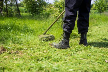 Bir adam benzin makası ile çimleri biçiyor. Seçici odak ile yakın plan.