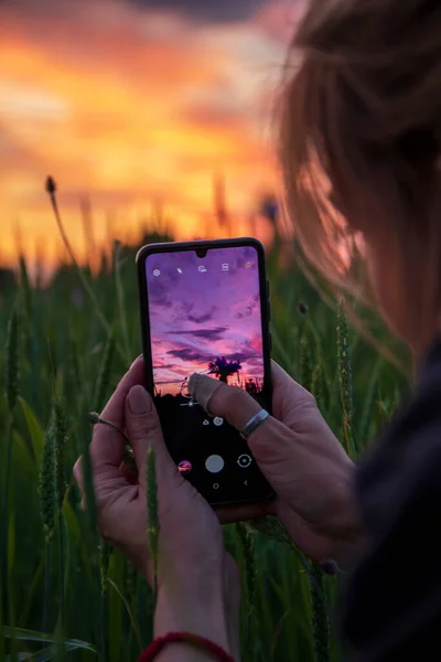 Kız cep telefonu kullanarak gün batımının fotoğraflarını çekiyor. Akıllı telefondaki fotoğraflar..