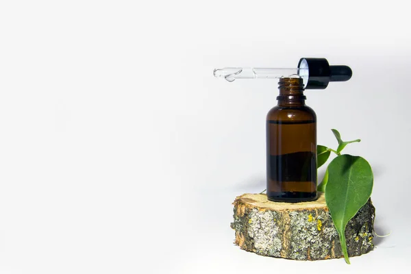 Eine Glasflasche braunen Serums mit einem Tropfer auf einem moosbedeckten Holzpodest. Spa kosmetisches Konzept. Platz für Ihren Text. Biokosmetik. Stockbild