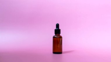 Pembe arka planda damlatan kahverengi cam şişe. Serum ya da gerekli yağ ambalajı. Kozmetik ürün Mockup.Boşluğu kopyala.