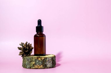 Pipetli kahverengi cam serum şişesi ve pembe arka planda, fotokopi alanı olan çam kozalağı. Vücut bakım serumu kozmetik cilt bakımı. Kopyalama alanı ile ön görünüm.