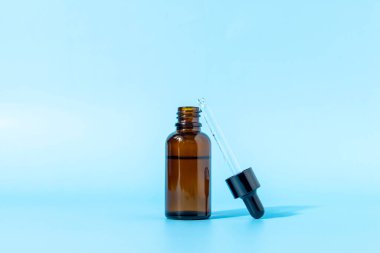 Mavi arka planda kahverengi camdan yapılmış cam damlatıcı şişenin gölgesi var. Kopya alanı ile ön görünüm. Kozmetik ürününün bir kopyası. Cilt bakımı için serum.