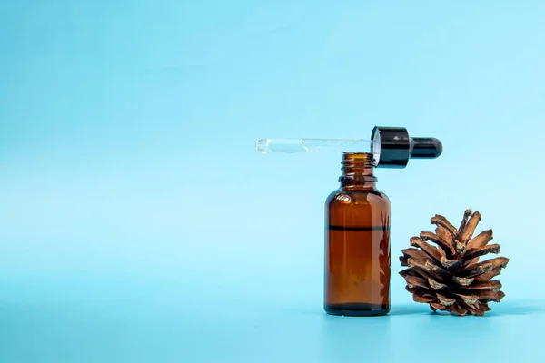 Brown glass serum bottle with pipette and pine cone on blue background with copy space. Body care serum cosmetic skin care. Front view with copy space. — Stock Photo, Image