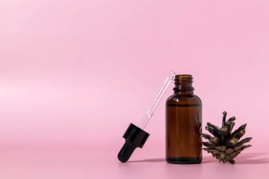 Pipetli kahverengi cam serum şişesi ve mavi arka planda çam kozalağı ve fotokopi alanı. Vücut bakım serumu kozmetik cilt bakımı. Kopyalama alanı ile ön görünüm.