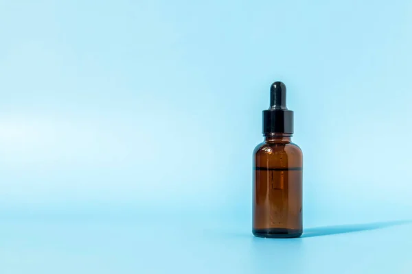 Mavi arka planda kahverengi camdan yapılmış cam damlatıcı şişenin gölgesi var. Kopya alanı ile ön görünüm. Kozmetik ürününün bir kopyası. Cilt bakımı için serum.