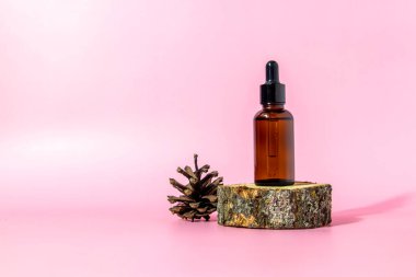 Pipetli kahverengi cam serum şişesi ve pembe arka planda, fotokopi alanı olan çam kozalağı. Vücut bakım serumu kozmetik cilt bakımı. Kopyalama alanı ile ön görünüm.