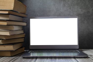 Kitap yığınının yanındaki masada açık bir dizüstü bilgisayar..