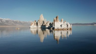 Kamera mavi göl yüzeyindeki beyaz taşlardan oluşan bir adanın etrafında hareket ediyor, 4K hava sahası.