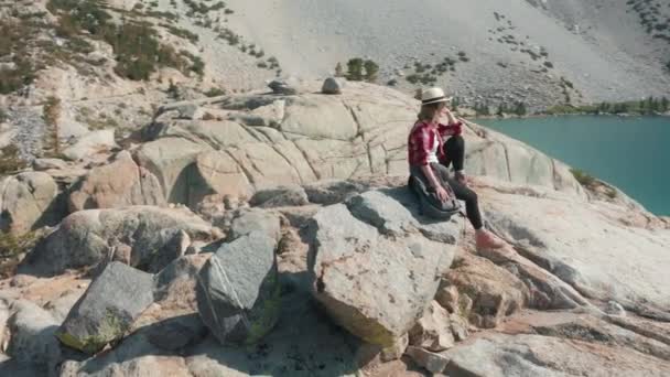 Frau genießt die Natur, sitzt auf einem hohen Felsen mit blauem See im Hintergrund — Stockvideo