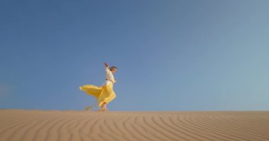 Kum tepesinde yürüyen neşeli bir kadın. Pozitif kız ellerle dengede duruyor