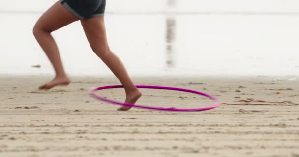 Kobieta kręcąca hula hoop używając jednej nogi na piaszczystej plaży — Wideo stockowe