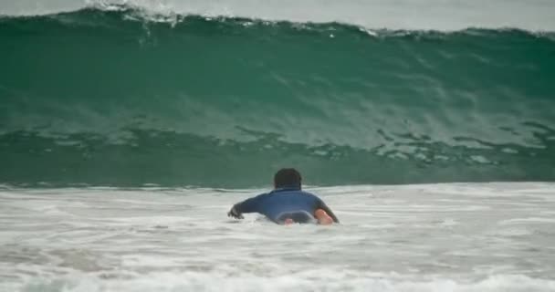 Wave rider laying onto the surfboard while swimming towards open water — Stock Video