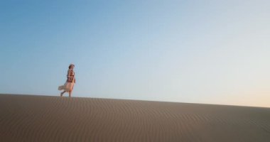 Gün batımında çölde kumulda yürüyen bir kadın. Neşeli kız ellerini kaldırıyor.