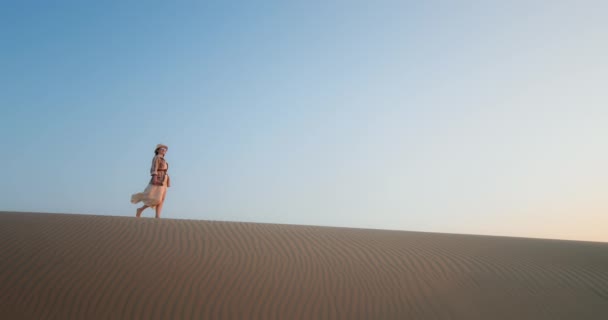 Dama caminando sobre dunas de arena en el desierto al atardecer. Chica alegre levantando las manos — Vídeos de Stock