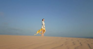 Ağır çekimde dalgalı kumda yalınayak yürüyen bir kadın.