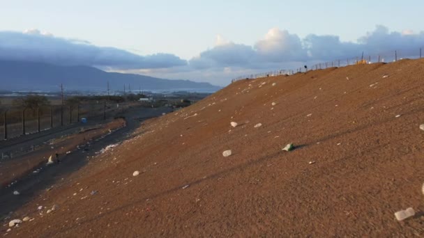 Fermer le reste des déchets plastiques volants avec le vent par la pente de la décharge au coucher du soleil 4K — Video