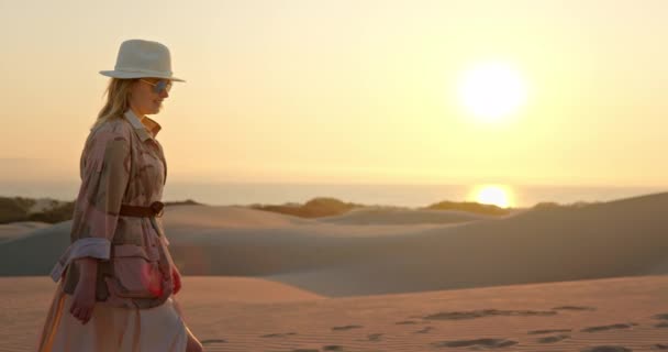 Femme souriante en chapeau marchant sur une dune de sable dans le désert — Video