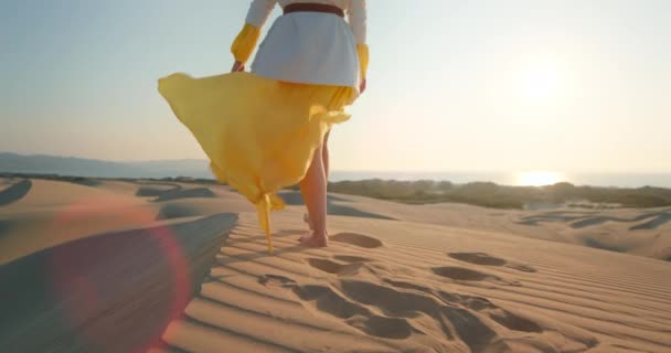 Mujer sexy en vestido amarillo saludando por el viento en el desierto. Señora caminando en la duna — Vídeos de Stock