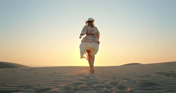 Kobieta biegnąca w kierunku zachodu słońca malowniczym krajobrazem pustyni 4K slow motion — Wideo stockowe