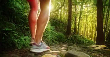 Kırmızı şortlu ve beyaz tişörtlü adam yosunlarla kaplı dik tepe boyunca yürüyor.