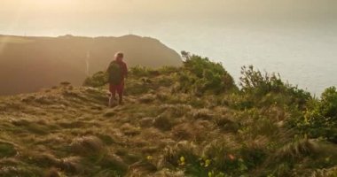 Sırt çantalı bir adam rüzgarlı tepede yürüyor.