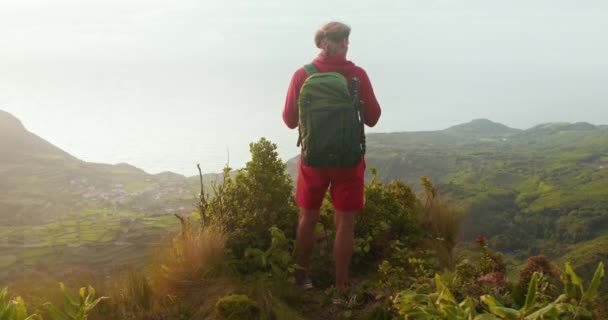 Мужчина турист с зеленым рюкзаком наслаждается красивыми пейзажами сельской местности. — стоковое видео