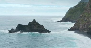 Yüksek gelgitlerle çevrili yosun ve bitki örtülü dik kayalıklar.