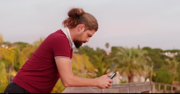 Widok z boku faceta opierającego się o poręcz podczas korzystania z telefonu komórkowego — Wideo stockowe