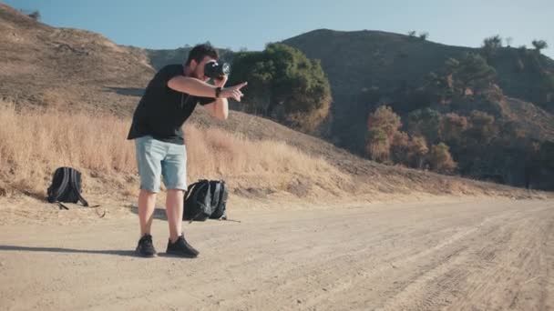 Man staat op stoffig pad, kijkt op camera en regisseert modellen, 4K — Stockvideo