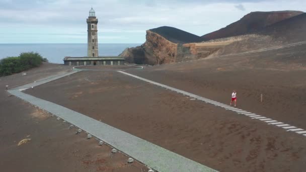 Sportsman correndo no caminho com o Centro de Interpretação de Vulcões de Capelinhos — Vídeo de Stock