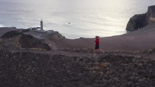 Jogger courir sur le sentier avec le volcan Capelinhos en arrière-plan, Faial Island — Video