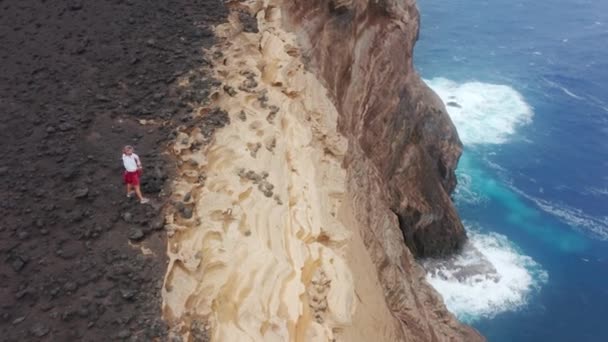 Filmagem aérea de um homem caminhando ao longo da borda do penhasco rochoso junto ao mar — Vídeo de Stock