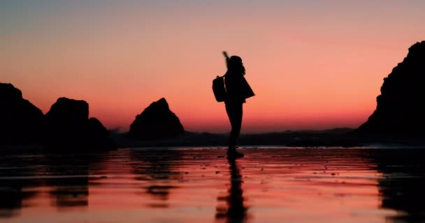 Okyanus sahilinde pembe turuncu gün batımı ışığında dans eden mutlu, heyecanlı kadın. — Stok video