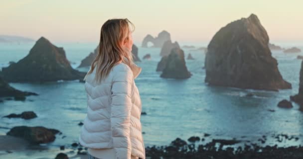 Young woman on ocean coast at sunset, looking around and breathing fresh air 4K — Stock Video