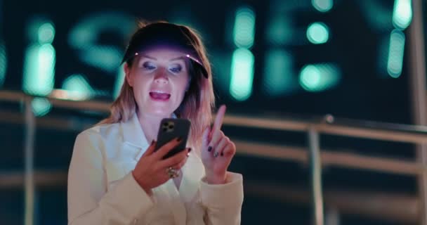 Mujer positiva aplicaciones de desplazamiento en su teléfono inteligente en las calles de la ciudad de noche 4K — Vídeos de Stock