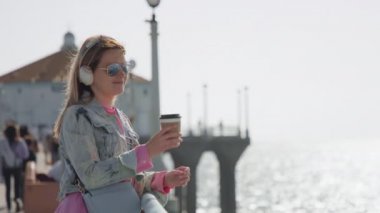 Happy smiling pretty woman enjoying coffee at the ocean pier with water view