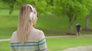 Back view of beautiful young woman listening music in wireless white headphones