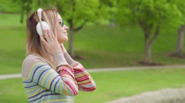 Young woman relaxing in green park on summer day in wireless white headphones 8K
