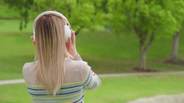 Frau in weißen Funkkopfhörern genießt den Morgen im grünen Stadtpark im Sommer — Stockvideo
