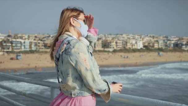 Frau im Freien am Strand der Stadt auf der Seebrücke bei Sonnenuntergang, mit Gesichtsmaske COVID 19 — Stockvideo