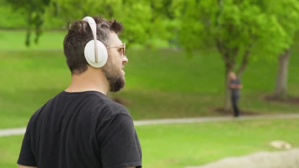 Rückansicht eines gutaussehenden jungen Mannes, der Musik in drahtlosen weißen Kopfhörern 8K hört — Stockvideo