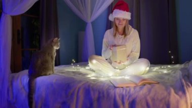 Kırmızı Noel Baba şapkalı mutlu kadın içinde sihirli ışık olan hediye kutusunu açıyor.