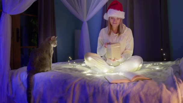 Ευτυχισμένη γυναίκα σε κόκκινο Σάντα Χριστούγεννα καπέλο άνοιγμα κουτί δώρου με μαγικό φως μέσα — Αρχείο Βίντεο