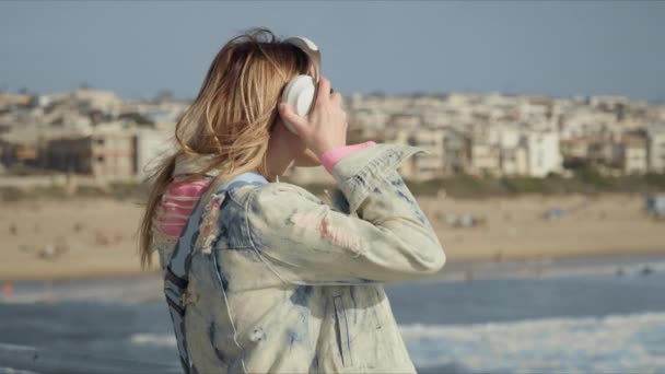 Mulher loira com fones de ouvido sem fio, ouvindo música, desfrutando do pôr do sol — Vídeo de Stock